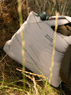 A light grey quilted tote bag from Wold & Weaver, shown outdoors on grass with a dark green drinks bottle and waterproof coat tucked inside.