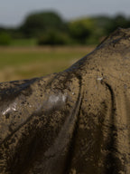 Close-up of a green waterproof country robe coat surface with wet rain water, set against a blurred Cotswolds countryside background of green grass and trees.